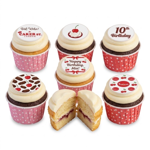 Six cupcakes with white frosting and cherry-themed edible toppers, some with vanilla sponge and some chocolate. One cupcake is cut open revealing jam filling.
