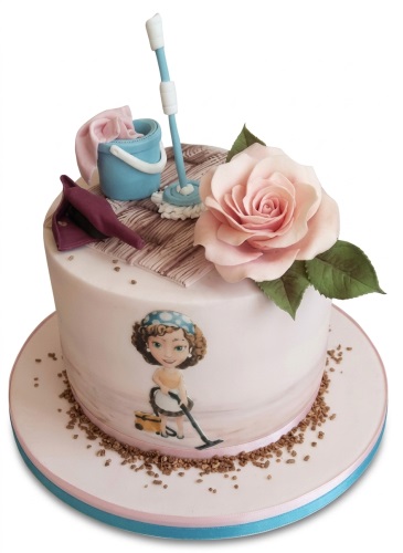 Round pink birthday cake with cleaning theme decorations, including a mop, bucket, vacuum cleaner woman, and a pink rose.