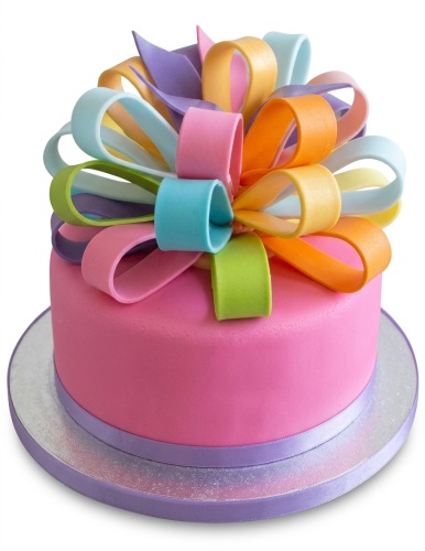 Round pink birthday cake with a large multi-coloured fondant gift bow on top.