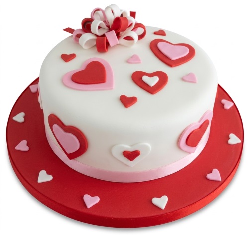 White round cake with red, pink, and white heart decorations and a ribbon bow.