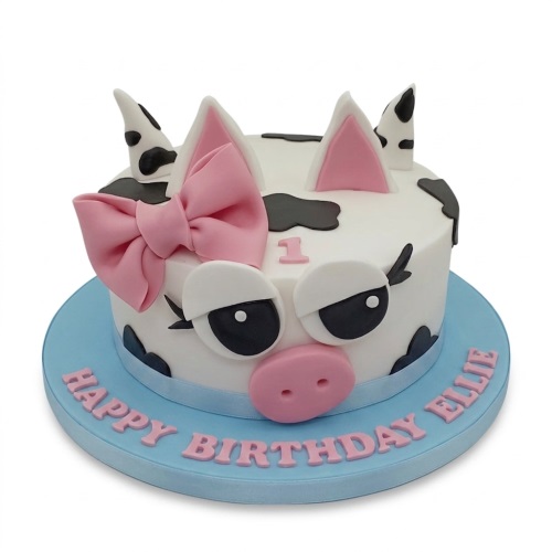White cow face birthday cake with pink bow, black spots, and a number one topper.