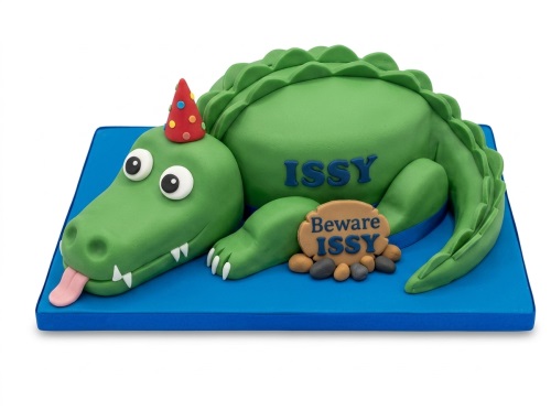 Green crocodile birthday cake with a red party hat on a blue board, with space for a custom name.