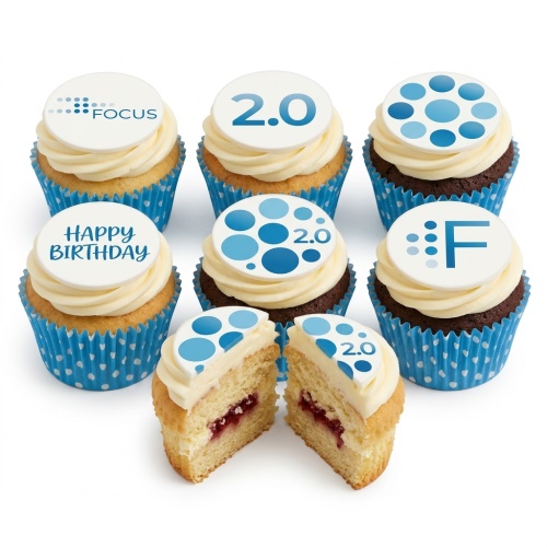Vanilla and chocolate cupcakes with white frosting and blue polka dot wrappers, topped with custom edible discs featuring 'Happy Birthday', 'FOCUS', '2.0', and abstract blue patterns.