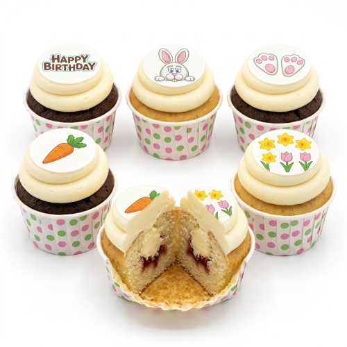 A selection of Easter-themed cupcakes with white frosting, decorated with a bunny, bunny feet, carrots, daffodils, tulips, and a 'Happy Birthday' message.