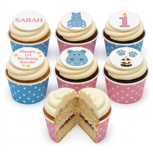 Cupcakes with white frosting in pink and blue polka dot cases, topped with blue hippos, a pink number one candle, paw prints with a cake, and example personalised messages.
