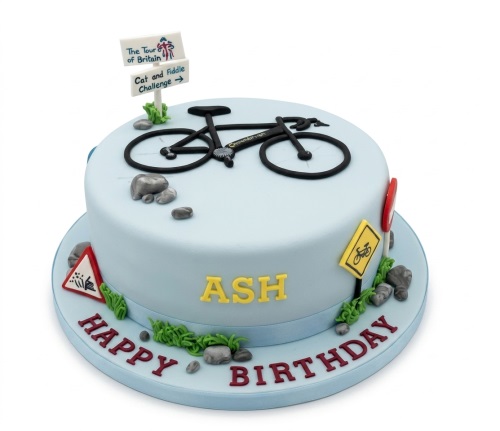 Light blue cycling theme birthday cake with black bicycle, road signs, and personalised name.