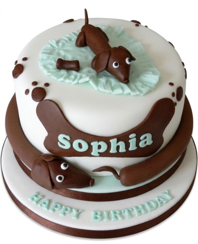Two-tier white and brown fondant cake with 3D dachshund dogs, paw prints, and a custom name plaque.