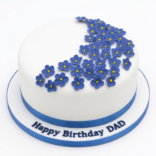 Round white birthday cake with blue fondant flowers and a blue ribbon.
