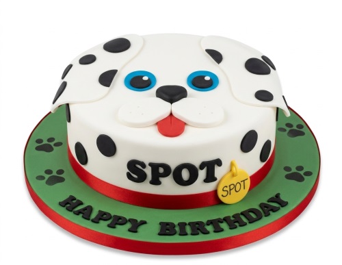 White dog face birthday cake with black spots, blue eyes, red tongue, and paw prints on a green board.