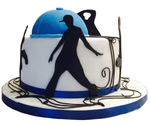 White round cake with black dancer silhouette, blue baseball cap, and musical swirls.