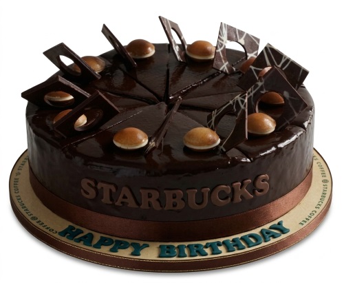 Round chocolate glazed cake with Starbucks logo, chocolate shards, and "Happy Birthday" on the board.