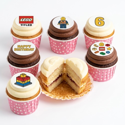 Selection of Lego theme birthday cupcakes with various toppers including Lego logo, minifigure, bricks, and a custom age '6' topper, in pink polka dot cases.