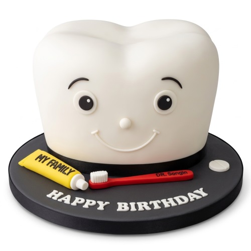 White smiling tooth cake with a yellow toothpaste tube, red toothbrush, and "Happy Birthday" message.