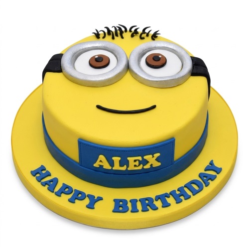 Yellow Minion birthday cake with silver goggles, black hair, and a blue band. The cake board has a blue plaque with a name and 'Happy Birthday' written on it.