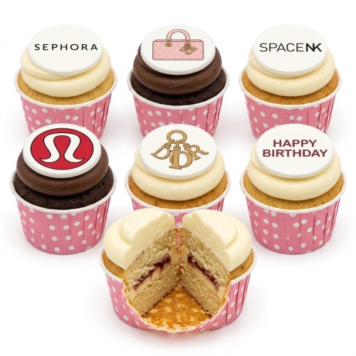 Cupcakes with white and chocolate frosting, topped with edible designer brand logos and a 'Happy Birthday' message, in pink polka dot cases.