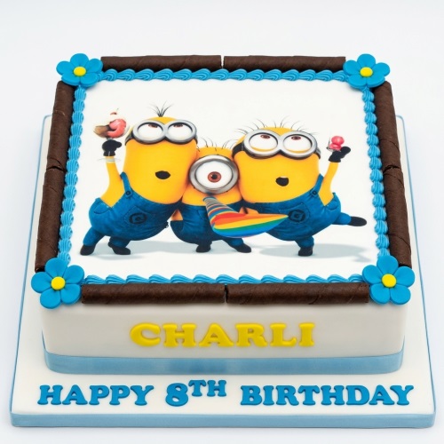 Square Minions birthday cake with three Minions characters, chocolate rolls, blue piping, and custom name and age.