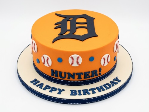 Round orange baseball theme birthday cake with blue 'D' logo, baseballs, and blue ribbon.