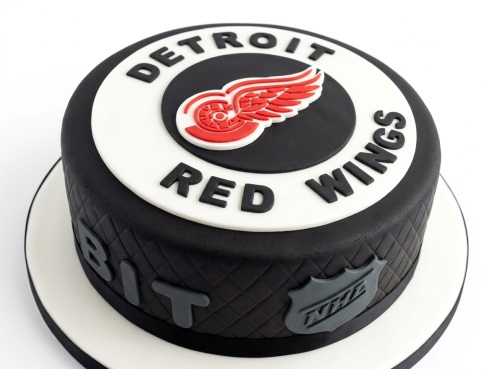 Round black ice hockey cake with Detroit Red Wings logo and NHL shield on the side.