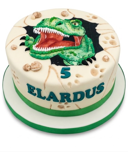 Round white birthday cake with a green dinosaur head breaking through a cracked egg design, featuring a custom age number and personalised name.