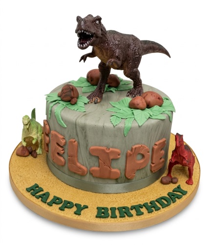 Round dinosaur birthday cake with T-Rex, smaller dinosaurs, green leaves, and custom name.