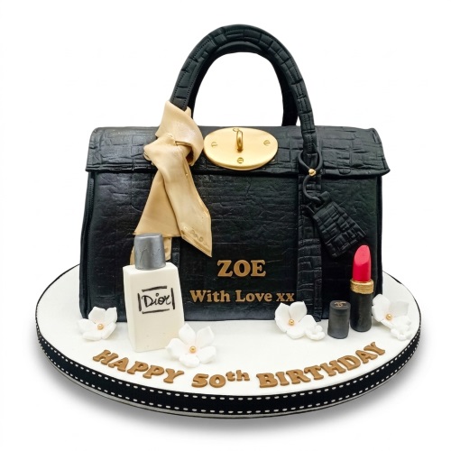Black designer handbag shaped birthday cake with gold clasp, scarf, perfume, lipstick, and white flowers.