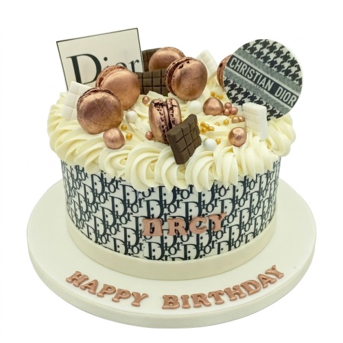 Round white cake with black Dior pattern, topped with cream, rose gold macarons, chocolate, and Dior logo toppers.