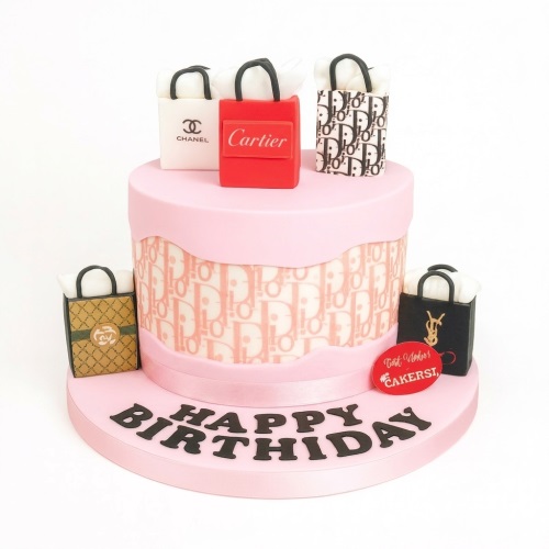 Two-tier pink birthday cake with edible designer shopping bags and "Happy Birthday" text.