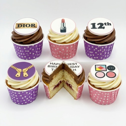 Assorted cupcakes with fashion and makeup themed toppers, including a Dior logo, lipstick, and zipper, with custom age.