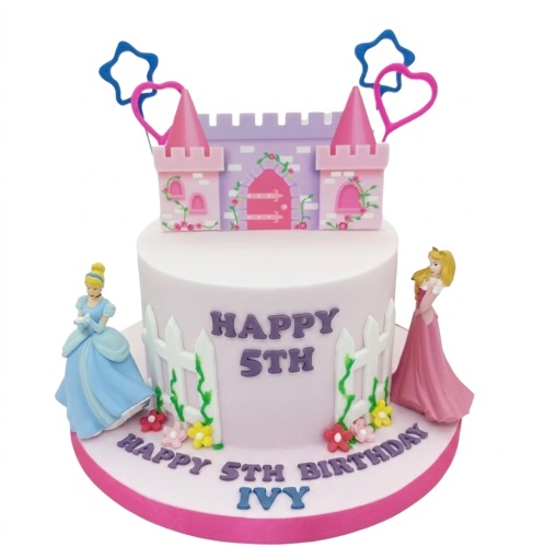 Round pink birthday cake with Disney Princess figurines, castle topper, fence, and flowers.