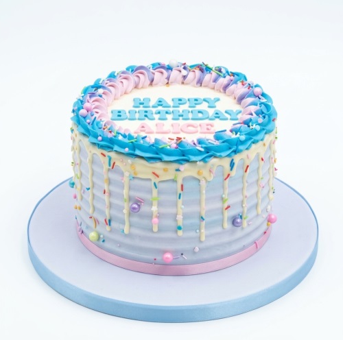 Round pastel drip birthday cake with white chocolate drip, sprinkles, and blue, pink, purple buttercream swirls.