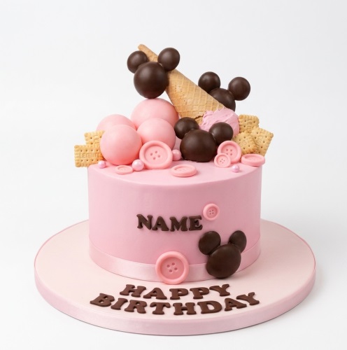Pink round birthday cake with chocolate Mickey Mouse heads, pink spheres, buttons, crackers, and an ice cream cone.