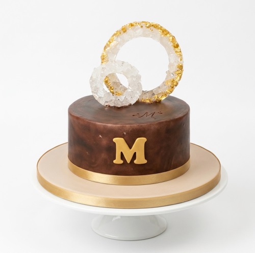 Elegant brown birthday cake with gold initial and crystalline gold-dusted rings