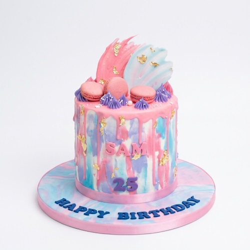 Pastel watercolour drip birthday cake with pink, blue, purple, gold leaf, macarons, and a custom age topper.