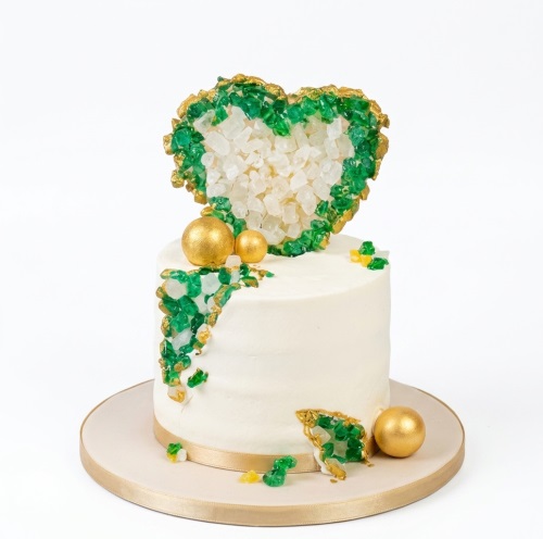 White cake with green and gold geode heart topper, cascading crystals, and gold spheres.