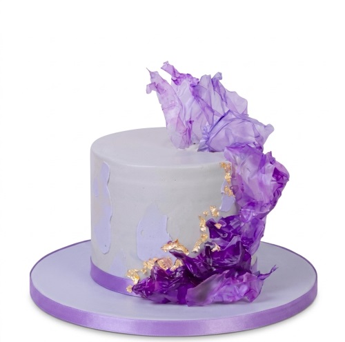 Single-tier purple and gold floral birthday cake with ruffled decorations and gold leaf.