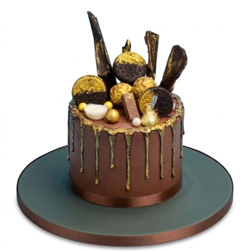 Single-tier chocolate cake with gold drip, chocolate shards, Oreos, Ferrero Rocher, Kit Kat, Hershey's Kiss, and pearls.