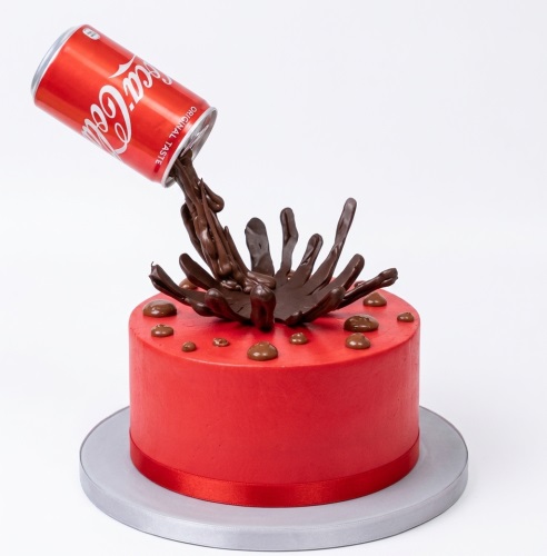 Red round birthday cake with an inverted Coca-Cola can spilling chocolate ganache.