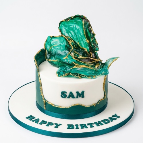 White and emerald green birthday cake with gold accents and a draped artistic topper.