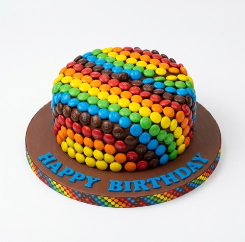 Round chocolate cake covered in colourful M&M's with a "Happy Birthday" message.