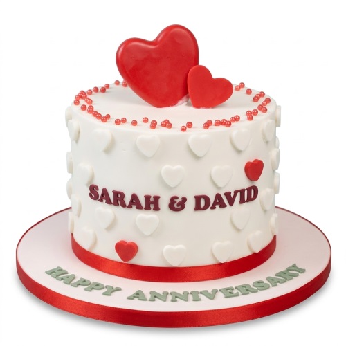 White anniversary cake with red and white hearts, red ribbon, and custom names.