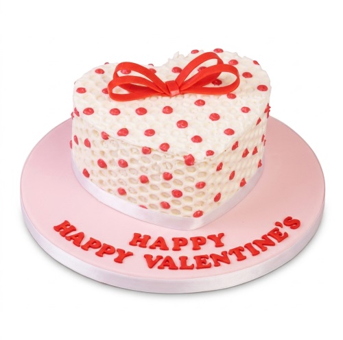 Heart-shaped white cake with red polka dots and a red bow on a pink board with "Happy Valentine's".