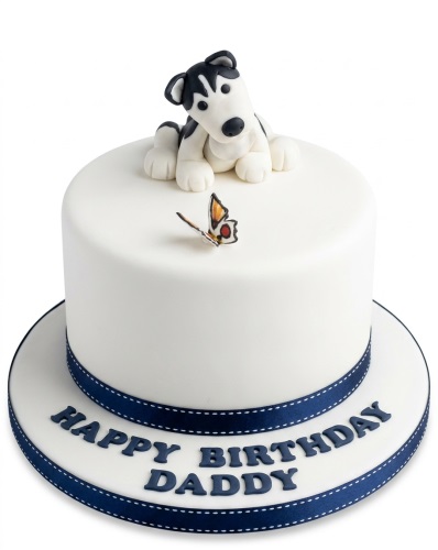 White round birthday cake with a black and white puppy figurine and a butterfly, with a blue ribbon and custom message.