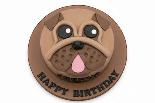 Round brown birthday cake decorated with a cute pug dog face, featuring black eyes, a black nose, and a pink tongue, with a personalised message on the board.