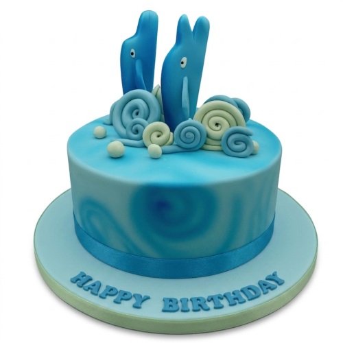 Round blue birthday cake with two dolphin figures, white swirls, and 'Happy Birthday' message.