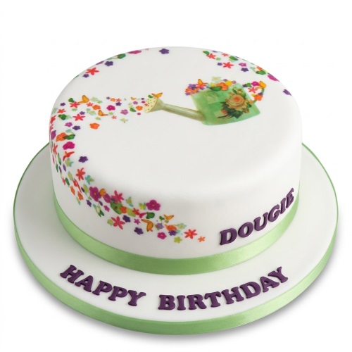 White round birthday cake with green watering can, colourful flowers, butterflies, and green ribbon.
