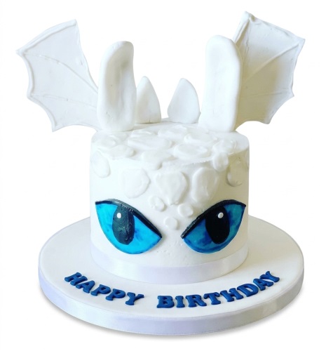 White dragon theme birthday cake with blue eyes and white wings, on a white cake board with 'Happy Birthday' message.
