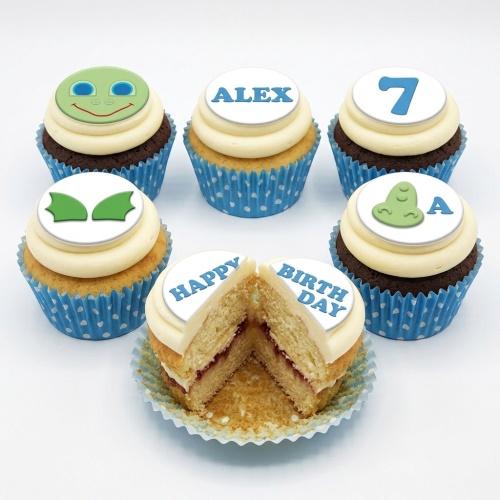 A set of cupcakes with white frosting and blue polka dot wrappers, featuring green monster-themed edible toppers and a custom age topper.