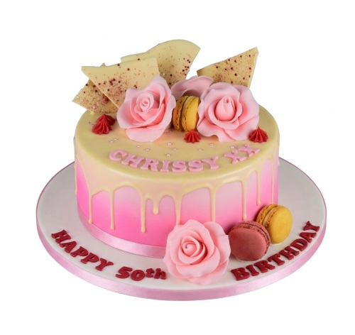 Round pink gradient drip cake with white chocolate shards, pink roses, macarons, and edible pearls.