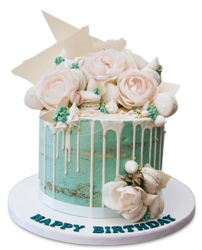 Mint green semi-naked drip cake with light pink roses, white macarons, and chocolate shards.
