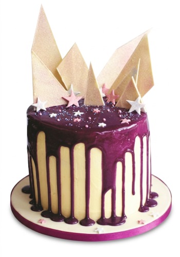 Round cake with purple drip, gold triangles, and pink and white stars.